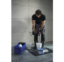 Řemeslník míchá lepidlo na obklady míchadlem ve vědru.