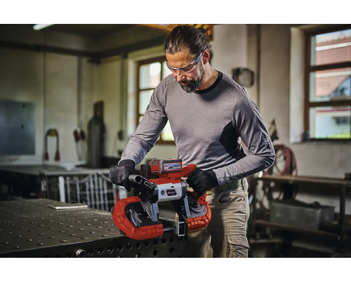 Muž řeže kov akumulátorovou pásovou pilou Einhell v dílně