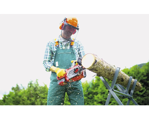 Muž řeže dřevo motorovou pilou na kozě, má na sobě ochranný oděv