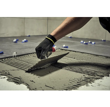 Dlaždič s hladítkem nanáší lepidlo na dlaždici, aby ji položil