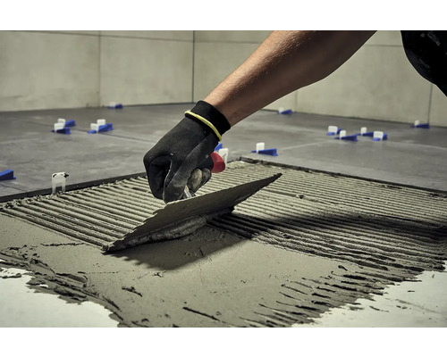 Dlaždič s hladítkem nanáší lepidlo na dlaždici, aby ji položil