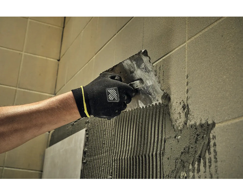 Obkladač nanáší lepidlo na stěnu pomocí špachtle