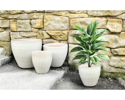 Skupina květináčů s rýhovaným povrchem a pokojová rostlina před kamennou zdí