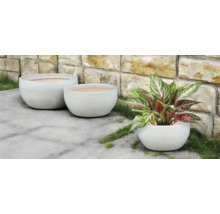 Tři kulaté květináče venku před kamennou zdí.