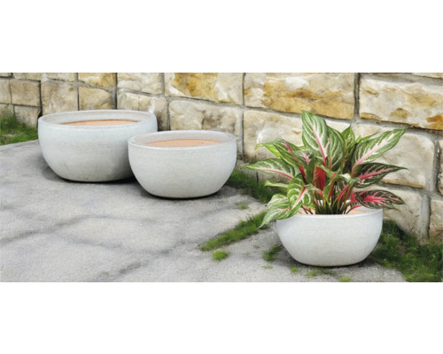 Tři kulaté květináče venku před kamennou zdí.