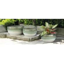 Tři kulaté keramické květináče na kamenné terase, z nichž jeden je s rostlinou.