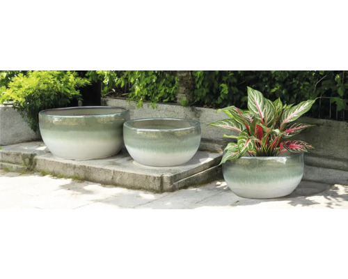 Tři kulaté keramické květináče na kamenné terase, z nichž jeden je s rostlinou.