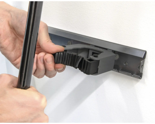 Osoba připevňuje nástroj k liště držáku nástrojů na zdi.