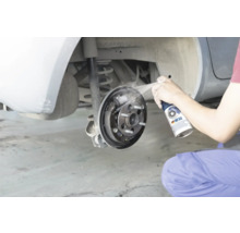 Osoba čistí otevřenou bubnovou brzdu automobilu čističem brzd.