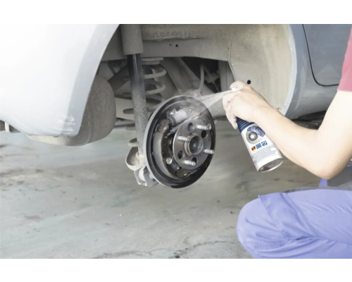 Osoba čistí otevřenou bubnovou brzdu automobilu čističem brzd.