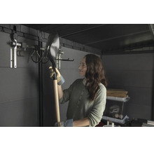 Žena drží lopatu v zahradním domku se systémem pro zavěšení nářadí