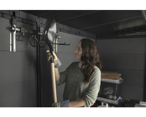 Žena drží lopatu v zahradním domku se systémem pro zavěšení nářadí