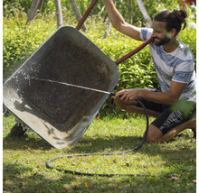 Muž čistí kolečko zahradní hadicí.