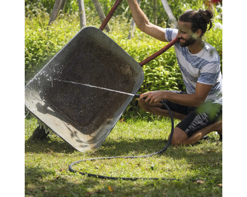 Muž čistí kolečko zahradní hadicí.