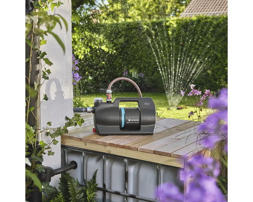 Zahradní čerpadlo Gardena na dřevěné konstrukci se zahradou v pozadí.