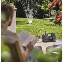 Zahrada se zahradním čerpadlem a zavlažovačem trávníku, zatímco si osoba čte knihu