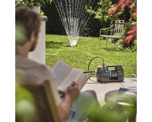 Zahrada se zahradním čerpadlem a zavlažovačem trávníku, zatímco si osoba čte knihu
