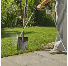 Osoba čistí zahradní rýč zahradní hadicí venku.