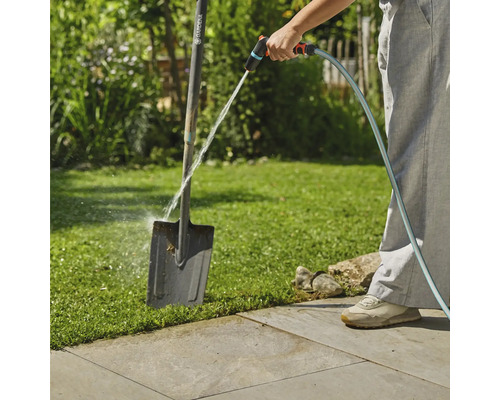 Osoba čistí zahradní rýč zahradní hadicí venku.