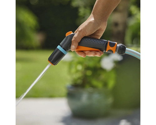 Ruka drží zahradní postřikovač Gardena, ze kterého vytéká voda.