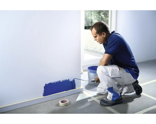 Muž maluje válečkem stěnu v místnosti.