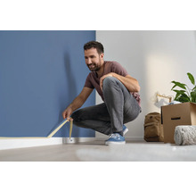 Muž lepí malířskou pásku na zeď, aby ji ochránil před cákanci barvy