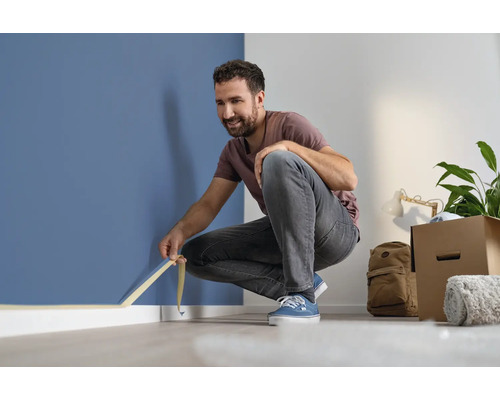 Muž lepí malířskou pásku na zeď, aby ji ochránil před cákanci barvy