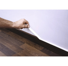 Ruka připevňuje soklovou lištu ke zdi nad laminátovou podlahou