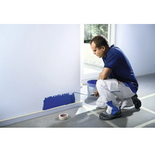 Muž maluje válečkem stěnu v místnosti.