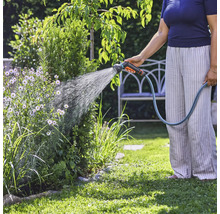 Osoba zalévá rostliny v zahradě zahradní hadicí.