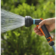 Ruka drží zahradní postřikovač, ze kterého stříká voda.