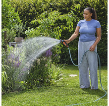 Žena zalévá rostliny zahradní hadicí na zahradě.