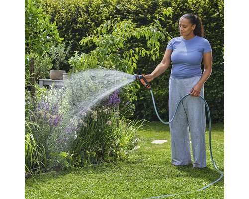 Žena zalévá zahradní rostliny zahradní hadicí a stříkací pistolí.