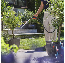 Osoba zalévá rostliny zahradní stříkací pistolí na zahradě.