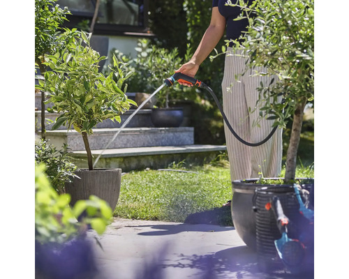 Osoba zalévá rostliny zahradní stříkací pistolí na zahradě.