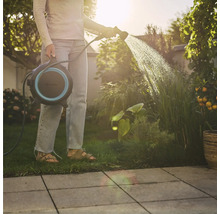 Žena zalévá rostliny hadicovým navijákem na zahradě.