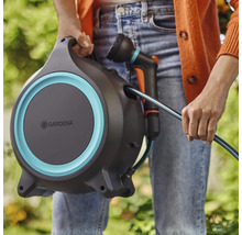 Osoba drží hadicový box Gardena se zahradní hadicí a postřikovačem.