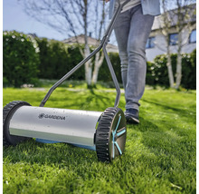 Ruční sekačka na trávu s osobou na zahradě.