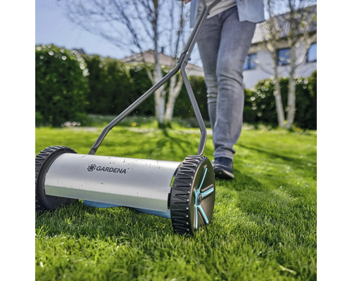 Ruční sekačka na trávu s osobou na zahradě.