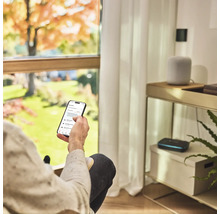 Osoba s chytrým telefonem pro ovládání zavlažování zahrady v obývacím pokoji.