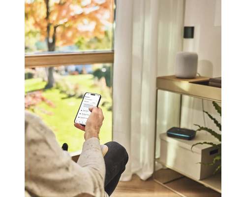 Osoba s chytrým telefonem pro ovládání zavlažování zahrady v obývacím pokoji.