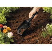 Zahradní lopatka v zemi s květinami v pozadí