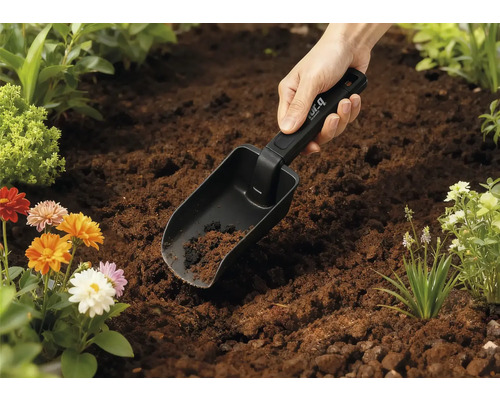 Zahradní lopatka v zemi s květinami v pozadí