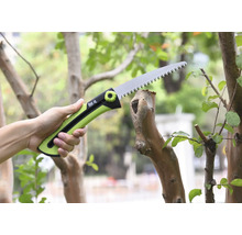 Ruka drží prořezávací pilu při řezání větve.