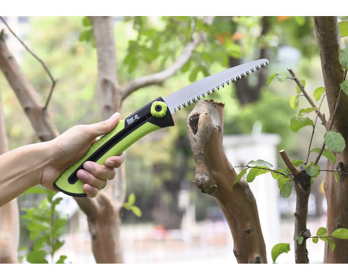 Ruka drží prořezávací pilu při řezání větve.