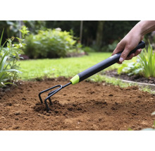 Detailní záběr ruky zatlačující zahradní kultivátor do půdy