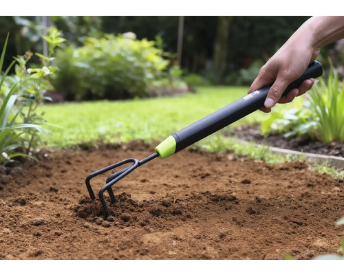 Detailní záběr ruky zatlačující zahradní kultivátor do půdy