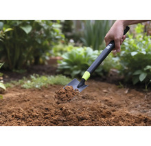 Ruční lopatka se zeminou držená na pozadí zahrady