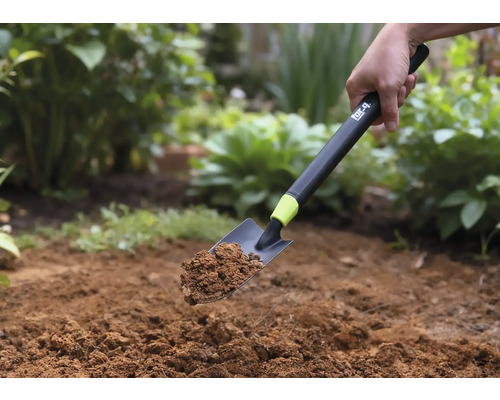 Ruční lopatka se zeminou držená na pozadí zahrady