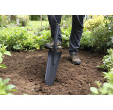 Osoba používá rýč k kopání v zahradě.